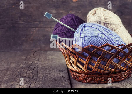 Knäuel Garn und Stricknadeln in einem Korb auf einem hölzernen Hintergrund gefärbt Stockfoto