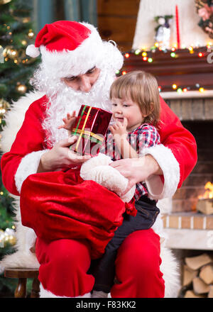 Glückliches Kind mit Geschenk auf Santa Claus Schoß Stockfoto