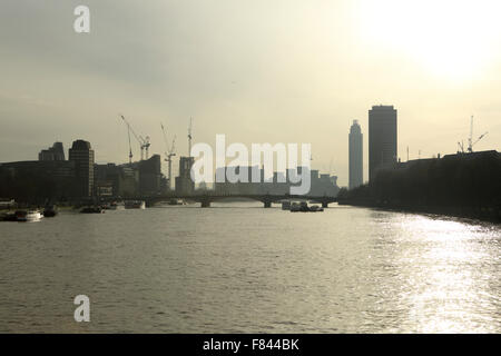 Sonne schimmert auf der Themse an einem trüben Tag in London, UK. Krane überragen am Flussufer Bauten von Lambeth Bridge. Stockfoto