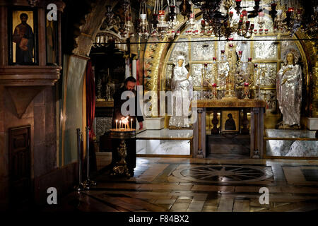 Ein griechisch-orthodoxer Priester zündet Kerzen vor dem Altar der Kreuzigung auf der linken Seite des Kalvarienberges oder Golgatha an, der traditionell als Ort der Kreuzigung Jesu angesehen wird. Der Hauptaltar gehört zu den griechisch-orthodoxen, die den Felsen von Golgatha 12. Station des Kreuzes in der Kirche des Heiligen Grabes Christian Quarter Old City East Jerusalem Israel enthält Stockfoto