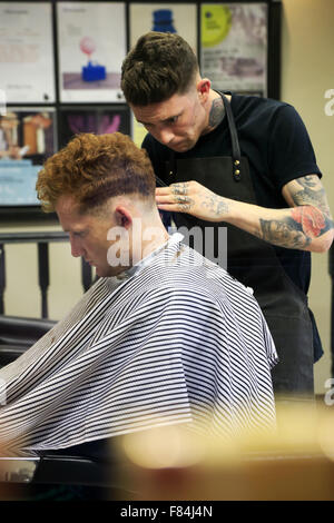 Ein Friseur in Zusammenarbeit mit seinen Kunden in einen Friseurladen. Dublin, Irland Stockfoto