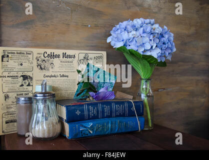 Bücher und Blumen auf einem Tisch in einem Café. Dieses Bild enthält Verweise auf Retro-Styling, Kaffee und Wiederverwendung, grün Stockfoto