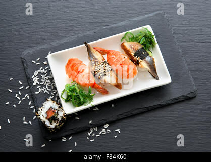 Sushi in Platte auf einem schwarzen Schiefer Tisch mit Salat Stockfoto