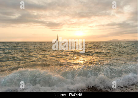 Segelboot Sonnenuntergang ist ein Segelboot segeln die Meere, während am Ufer eine goldene Ozeanwelle abstürzt. Stockfoto