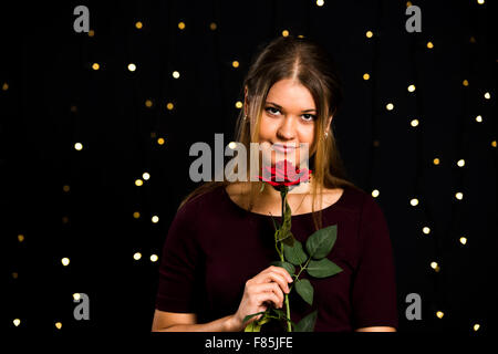 junge hübsche Frau auf schwarzem Hintergrund mit roten rose Stockfoto