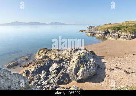 Vulkangestein und Strand auf Llanddwyn Island, Anglesey, Wales mit Halbinsel Llyn im Hintergrund Stockfoto