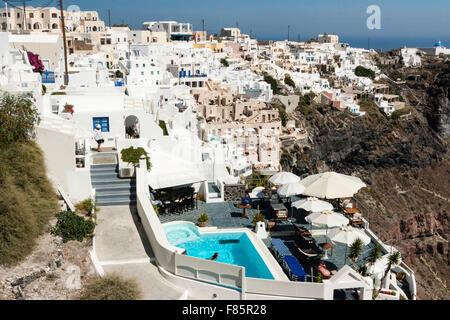 Santorini. Hotelkomplex mit Terrasse Pool und Sitzecke, Hintergrund, Dorf Imerovigli mit cubiform weiße Gebäude auf einer Klippe. Stockfoto