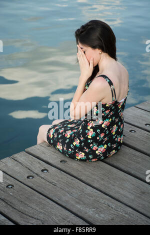 Elende junge Frau verbirgt ihr Gesicht auf dem Steg am Meer Stockfoto