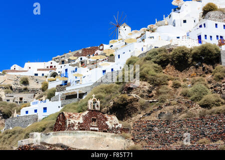 Santorini, Oia Stadt. Blick hinauf auf den weiß getünchten Gebäuden cubiform in die Felsen gebaut, mit typischen Mühle am Horizont gegen den klaren blauen Himmel. Stockfoto