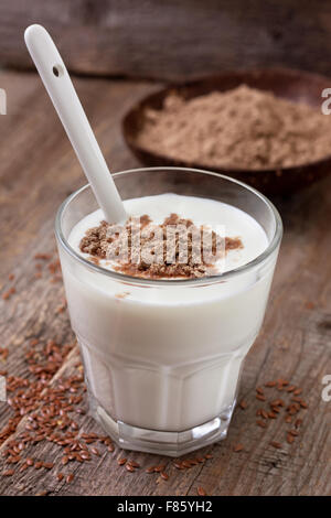 Glas Joghurt mit zerquetschten Leinsamen, Leinsamen Mehl in einer Holzschale auf einem hölzernen Hintergrund Stockfoto
