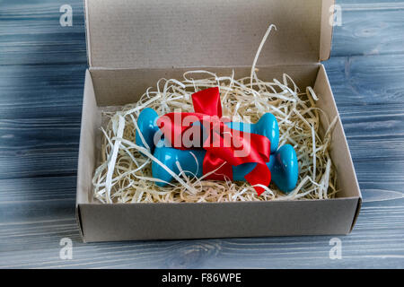 Zwei blaue Hanteln in Geschenkbox mit roten Band auf dem hölzernen Hintergrund. Stockfoto