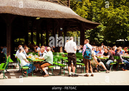 München, Deutschland - Leute sitzen in der Sonne auf den Bänken der chinesischen Turm Biergarten am Englisher Garten in München Stockfoto