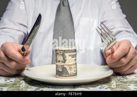 Geschäftsmann sitzt hinter einem Tisch mit Gabel und Messer bereit, ein Bündel von Dollar Essen serviert auf Teller - Business-Konzept Stockfoto