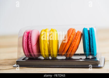 Bunte Makronen in Kunststoff-Box auf Holzboden Stockfoto