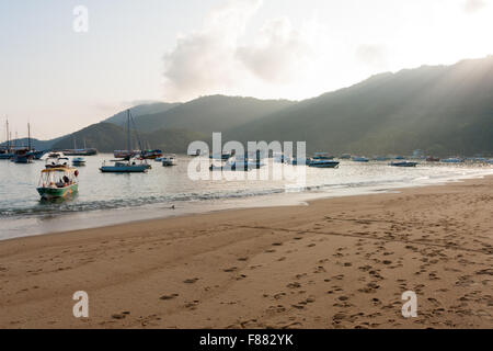 Sonnenaufgang mit Sonnenstrahlen, die durch die Berge. Boote in Vila do Santorini, Ilha Grande, Angra dos Reis, Bundesstaat Rio de Janeiro, Brasilien Stockfoto