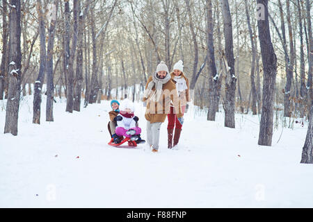 Glücklicher Mann Reiten Kinder auf Schlitten im Winter park Stockfoto