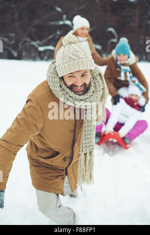 Glücklicher Mensch in Winterbekleidung reiten seinen Sohn und Tochter auf Schlitten im winter Stockfoto