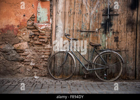 Altes Fahrrad geliehen gegen eine notleidende Holztür In den Straßen von Marrakesch Stockfoto