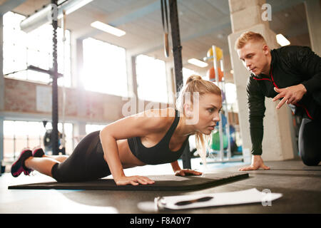 Innenaufnahme des jungen weiblichen Training mit personal Trainer im Fitness-Studio. Fitness-Frau tut Push Ups mit ihrem persönlichen Trainer bei h Stockfoto