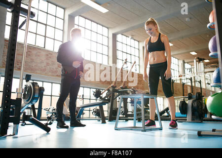 Aufnahme einer jungen Frau, Turnen in der Turnhalle mit der Aufsicht eines personal Trainers. Stockfoto