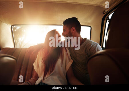 Glückliches Paar Road trip. Junger Mann und Frau sitzen auf der Rückbank des Autos sahen einander lächelnd an einem Sommertag. Stockfoto