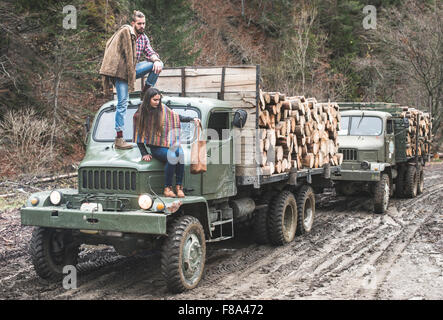 Junger Mann und Mädchen auf LKW mit Baumstämmen im Wald Stockfoto
