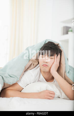 Müde Menschen bedeckt mit einer Bettdecke mit geschlossenen Augen auf dem Bauch auf dem Bett liegend Stockfoto