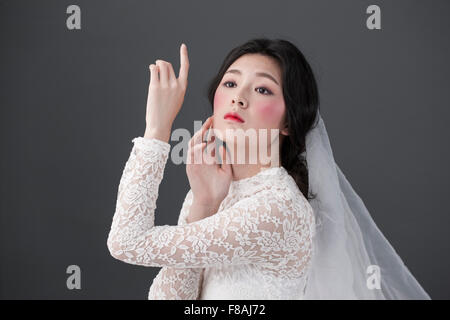 Asiatische Frau im weißen Spitzenkleid und Spitzenschleier mit rosa Blush Make-up starrte nach oben mit keinen Gesichtsausdruck und berühren Stockfoto