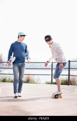 Junger Mann in eine schwarze Kappe, skateboarding und der andere Mann in eine blaue Kappe mit seinem Skateboard unter dem arm Stockfoto