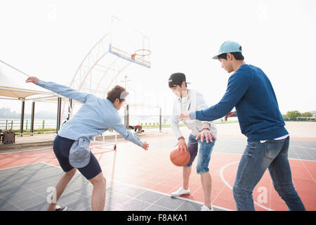 Drei junge Männer am Hof Basketball spielen Stockfoto