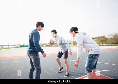 Drei junge Männer auf der Suche nach unten und Basketball aktiv am Hof zu spielen Stockfoto