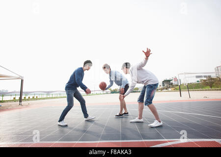 Drei junge Männer Basketball aktiv am Hof zu spielen Stockfoto