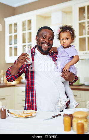 Glücklicher afrikanisch-amerikanischer Mann mit Glas Milch hält seine kleine Tochter Stockfoto