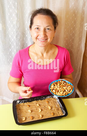 Reife Frau fügt Muttern zu Teig verarbeiten. Eines der Stadien des Kochens des Honigkuchen.  Serien ansehen Stockfoto