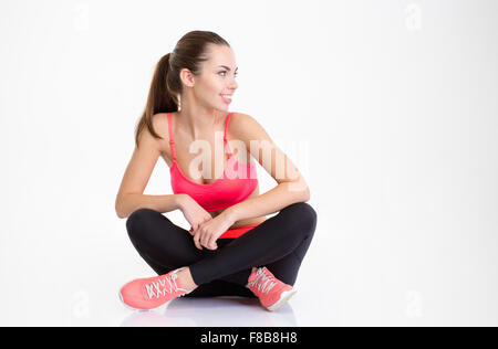 Glücklich lächelnden jungen Fitness Frau sitzt mit gefalteten Beinen und schauen Weg über weißen Hintergrund isoliert Stockfoto