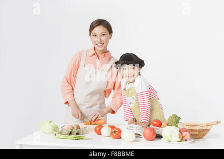 Mutter und Tochter in Schürzen stehen am Tisch zusammen und kochen zusammen starrte mich mit einem Lächeln Stockfoto