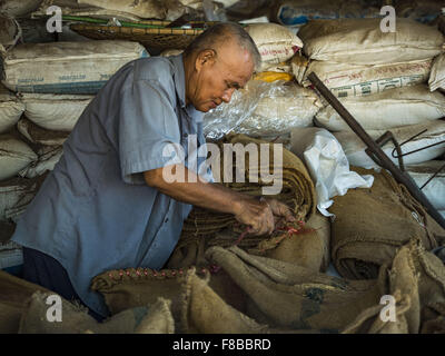 Nong Saeng, Nakhon Nayok, Thailand. 8. Dezember 2015. Ein Arbeiter in einem Reis, die Trocknung Geschäft näht geschlossen Taschen trocken aber unmilled Reis während der Reisernte in der Provinz Nakhon Nayok, etwa zwei Stunden nördlich von Bangkok. Thailändische landwirtschaftliche Beamte erwarten Reis Preise von weniger als 15 % steigen, da die weltweite Produktion von Reis durch den Pazifischen Ozean El Niño Wettermuster geschnitten wird. Thailands Reisproduktion wird voraussichtlich im kommenden Jahr fallen. Anhaltende Trockenheit hat die Hauptkultur, derzeit geerntet, reduziert und die Militärregierung hat Landwirte keine zweite Ernte '' Trockenzeit '' Pflanzen bestellt Stockfoto