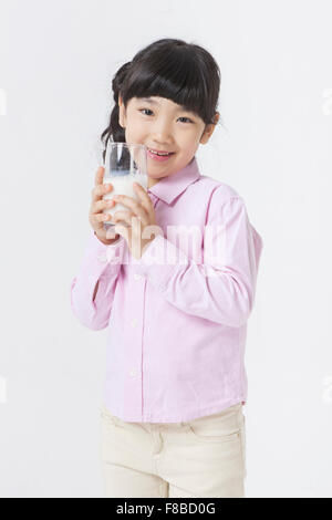 Mädchen mit Pony Tail Frisur in rosa t-Shirt hält ein Glas Milch in der Nähe von ihrem Gesicht und Lächeln Stockfoto