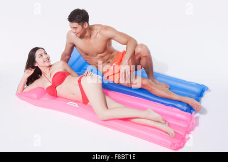 Hohen Winkel muskulöser Mann in Baden Hose und Frau im roten Bikini sowohl auf Wagen liegend und sahen einander mit einem Lächeln Stockfoto