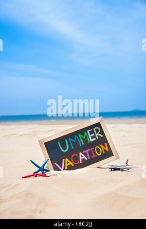 Wort geschrieben am Holzrahmen in verschiedenen Farben mit Seestern und Miniatur-Fläche auf Sand vor dem Hintergrund der Sommerferien Stockfoto