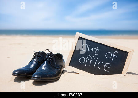 Mannes Geschäft Schuhe mit Out of Office Word geschrieben in Holzrahmen mit dem Hintergrund des Strandes in Sand stecken. Stockfoto