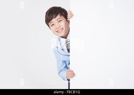 Grundschule Alter Junge in Schuluniformen versteckt sich hinter einer weißen textfreiraum und lächelnd Stockfoto