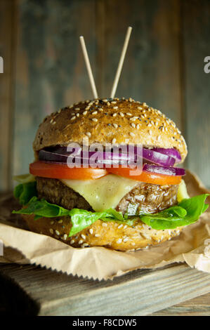 Gourmet-Burger mit Käse, Tomaten und Zwiebeln füllen oben auf ein Schneidbrett aus Holz Stockfoto