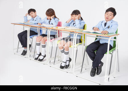 Vier Grundschüler in Schuluniformen am Schreibtisch zu sitzen müde und gelangweilt Stockfoto