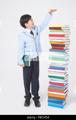 Grundschule junge in der Schule Uniformen ein Buch hält und Gestikulieren, Messen der Höhe von einem Stapel von Büchern Stockfoto