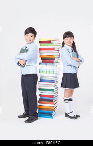 Grundschule-jungen und Mädchen in Schuluniformen stehen Rücken an Rücken mit einem Stapel Bücher zwischen Ihnen Stockfoto