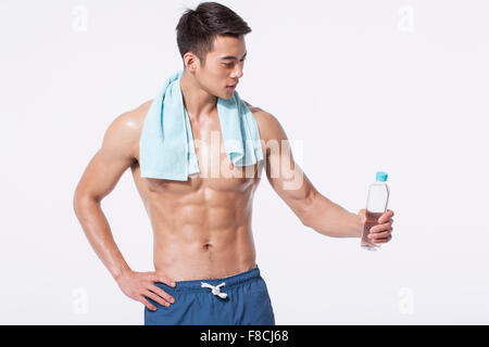 Muskulöser Mann mit einem Handtuch um den Hals hält eine Flasche Wasser und auf der Suche nach unten mit der Hand auf den Bauch Stockfoto