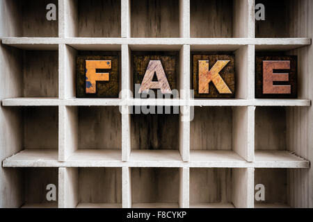Das Wort "FAKE" in Vintage Tinte befleckte hölzerne Buchdruck-Typ in einen partitionierten Drucker Schublade geschrieben. Stockfoto