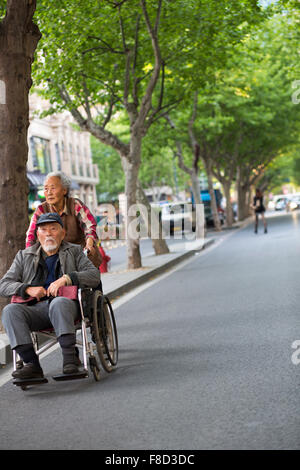 Frau treibt einen Alter Mann im Rollstuhl auf der Straße von Shanghai Stockfoto