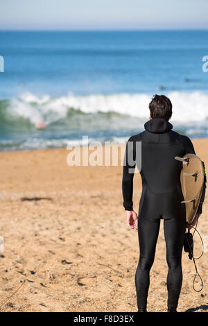 Junge Surfer Mann stehend an einem Strand und Durchführung seiner Surf board Stockfoto